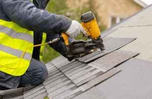 worker with a nail gun putting shingles on a roof